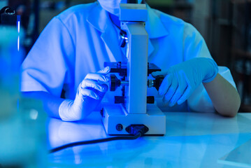 Woman scientist in lab look at science microscope medical test researching biology chemistry in blue light black background. Female technician laboratory analyze genetic research. Chemistry Medical