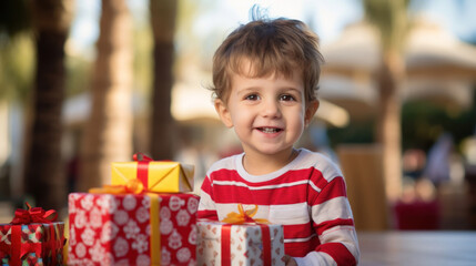 Fototapeta na wymiar A cheerful toddler boy with a beaming smile, surrounded by a variety of wrapped birthday presents, in an outdoor setting.