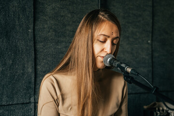 Woman singer play piano and sing in microphone, recording song in sound record studio.
