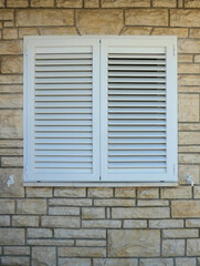 white aluminum external window shutters against stone brick wall  