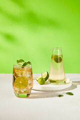 Two glasses of detox water with kumquat and fresh lemon are displayed on a white surface with a green background. Space viewed from the front.