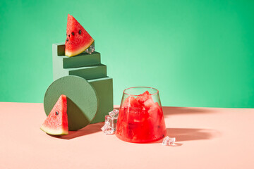 A glass of watermelon juice with ice and fresh watermelon next to the green platform. Copy space...