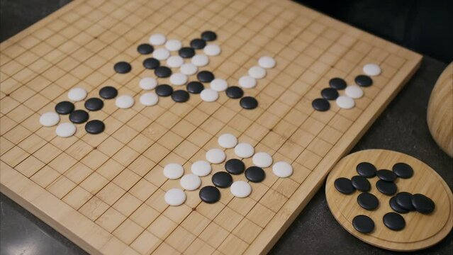 Overhead 45 degree view of man's hand placing a white stone in the middle of the ancient Chinese board game Go on a bamboo wooden board with black pieces scattered in the foreground