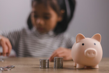 Little Asian girl saving money in a piggy bank, learning about saving, Kid save money for future...
