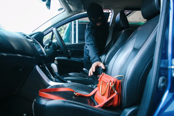 A thief in a robbery mask stealing a purse bag in a car - obrazy, fototapety, plakaty