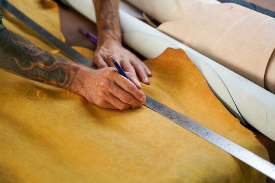 Closeup and crop hands of leather craftsman using a pencil and steel ruler drawing design on the yellow leather in the workshop. - Powered by Adobe