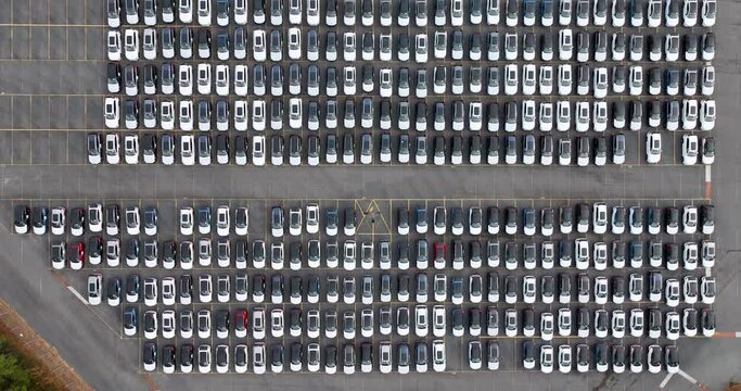 Aerial view of a new car lot, neatly arranged vehicles reflecting uniformity and precision, symbolizing organized commerce and transportation.