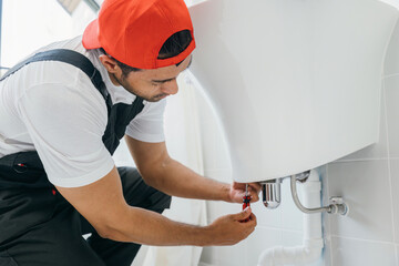 A technician in action repairs a water pipe under a bathroom sink. This skilled plumber emphasizes fixing leaks cleaning clogged pipelines and improving plumbing for efficient service.