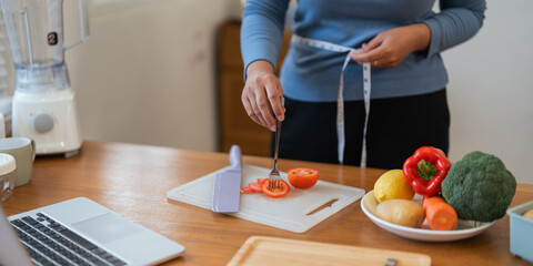 Young woman asian measure her waist in the kitchen the with vegetables and fruits. Concept of healthy eating and dieting