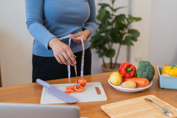 Obraz na płótnie Canvas Young woman asian measure her waist in the kitchen the with vegetables and fruits. Concept of healthy eating and dieting