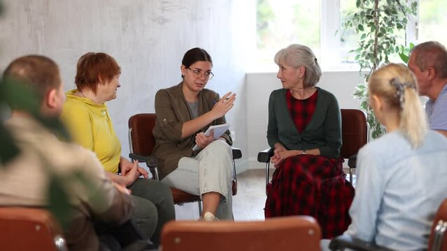 Young woman presides over support group meeting with mature people listening . High quality 4k footage