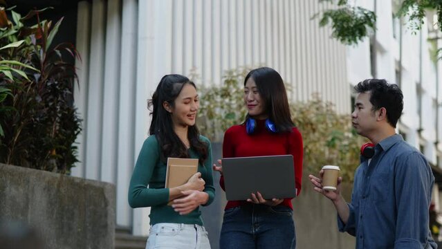 Classmate student friend standing on walkwayand talk about learning content subject in classroom on laptop within university or high school