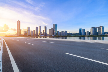 Asphalt highway road and river with modern city buildings at sunrise