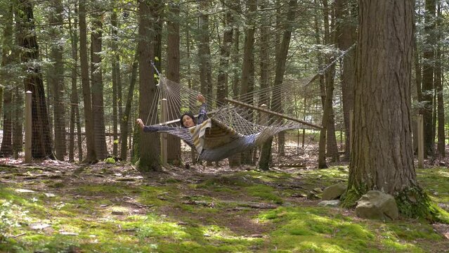 Young adult female stretching and swinging in woodland hammock enjoying relaxed lifestyle