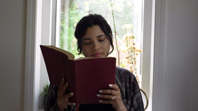 Puerto Rican young adult female reading holy bible at home inspired by scripture