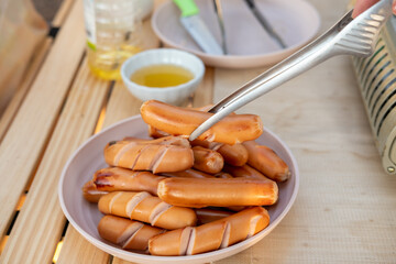 A woman's hand is holding sausages and placing them on a plate. While going camping to relax