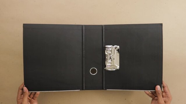 Holding open black lever arch file with ring binder on office desk.
