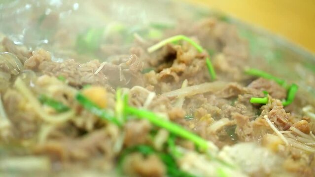 황동색 불고기 냄비에 양념 불고기와 팽이 버섯을 올리고 부추와 육수를 부어 넣고 끓이는 