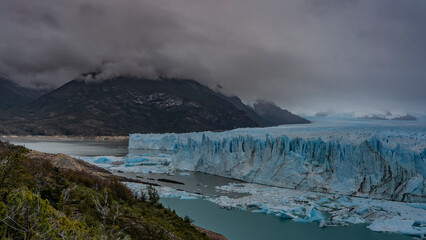 The breathtaking landscape of the Perito Moreno Glacier. An array of blue ice stretches to the horizon between the mountains. A glacial wall with cracks and sharp peaks rises above the lake. Fog. 