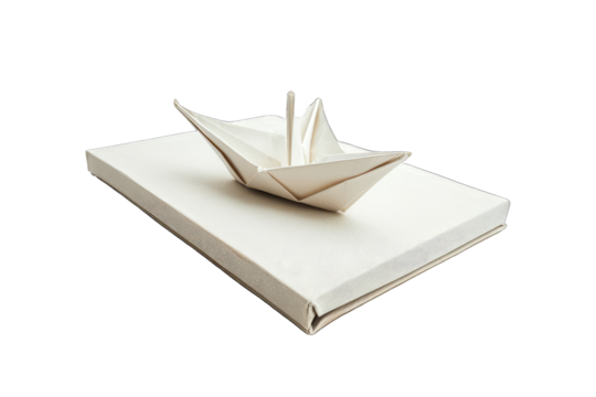 white origami paper boat placed on top of a closed book with a canvas cover