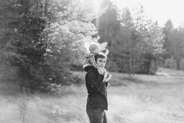 Dad with a little girl on his shoulders stands in a clearing in the forest. Black and white photo....