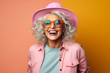 Portrait of a happy senior woman in hat and sunglasses over orange background