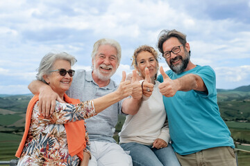 Happy multi generation family having fun together on outdoor countryside excursion, gesturing thumbs up to the camera. Parents, son and daughter-in-law enjoying free time and recreational activities