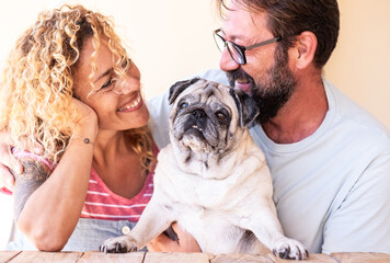 Beautiful middle aged couple man and woman in love share tender moment with their clear pug dog....