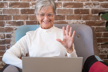 Video call concept. Happy senior retired woman waving hands video calling by laptop, old white...