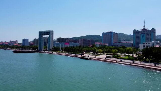 Aerial dolly view Xingfu park flying from sea side flying toward the city - Weihai China