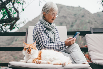 Defocused senior woman sitting outdoors on a chaise longue in the company of her beautiful cat....