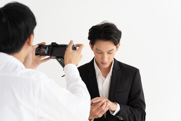 Asian groom in a stylish suit meticulously adjusts his cufflinks as a photographer captures the moment. Elegance in focus: a professional photographer takes a groom's portrait - Powered by Adobe