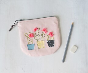 Pink handmade zipper pouch with cute cacti in pots , grey pencil and white eraser over white	