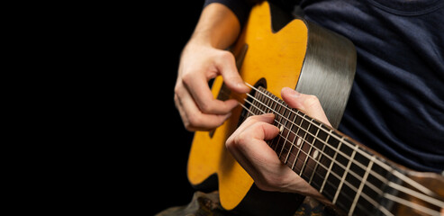 Man plays an acoustic guitar on a black background. The musician clamps the frets of the guitar on...