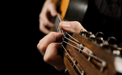 Playing an acoustic guitar on a black background. The musician clamps the frets of the guitar on...