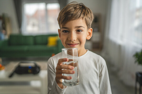 One boy caucasian kid stand at home hold glass of water thirsty drink