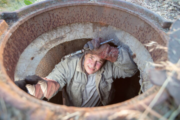 Sewage works. Industrial wastewater treatment. A worker in a sewer hatch with a plumbing key.