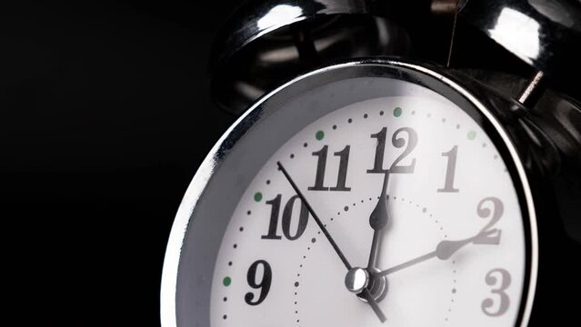 Close-up of a retro alarm clock face in time lapse on black background. Retro alarm clock running fast. Clock hands move fast, the beginning of time 12:00 AM or 12:00 PM.