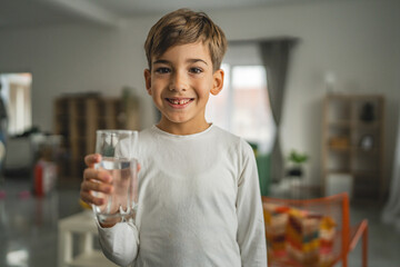 One boy caucasian kid stand at home hold glass of water thirsty drink