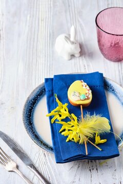 Easter table setting with blue napkins, burgundy water glasses and yellow decor on a wooden table. Easter lunch concept.