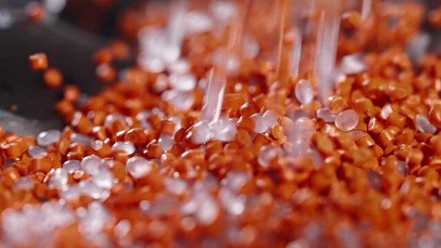 Macro frame of white and orange plastic granules. The polymer composite is poured into a tank for further production and casting in special molds. Production
