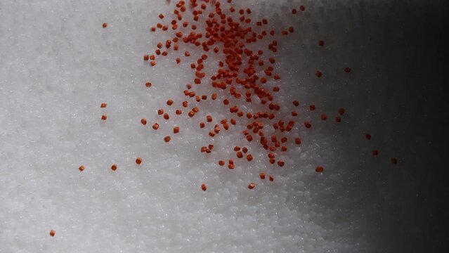 Macro frame of white and orange plastic granules. The polymer composite is poured into a tank for further production and casting in special molds. Production