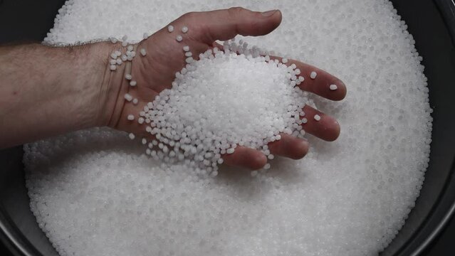 A factory worker checks plastic pellets before they are put into production. White compound in a man's hand. Production