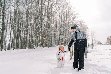 Fototapeta na wymiar Mom looks at the little girl standing in a snowdrift on a snowy road, holding hands