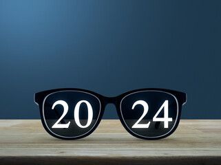 2024 white text with black eye glasses on wooden table over light blue wall, Business vision happy new year 2024 cover concept