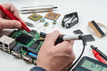 Close up of a technician's hands in a workshop. Repairer is soldering circuit board of electronic...