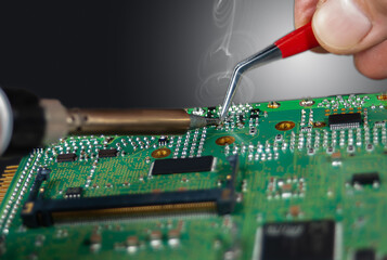 Close up of a technician's hands in a workshop. Repairer is soldering circuit board of electronic...