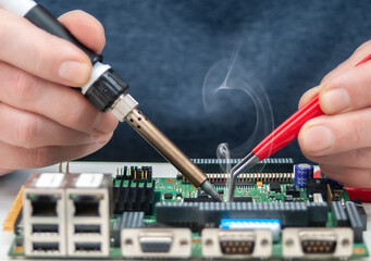 Close up of a technician's hands in a workshop. Repairer is soldering circuit board of electronic...