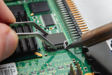 Close-up of a technician's hands in a workshop. The repairer is soldering an IC in a PLCC package...