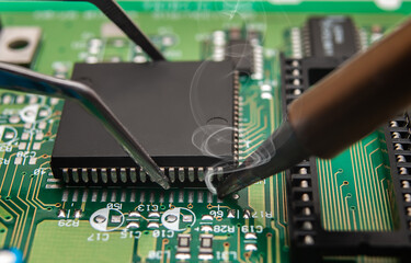 Close-up of a technician's hands in a workshop. The repairer is soldering an IC in a PLCC package...